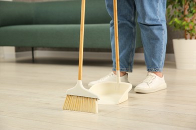 Photo of Woman with broom and dustpan cleaning floor indoors, closeup