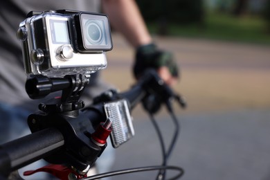 Man riding bicycle with modern action camera outdoors, closeup. Space for text