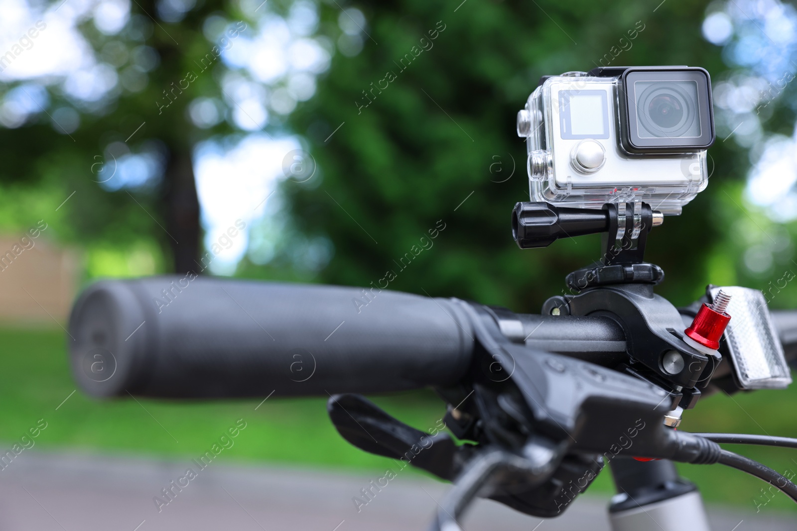 Photo of Modern action camera with mount on bicycle outdoors, closeup