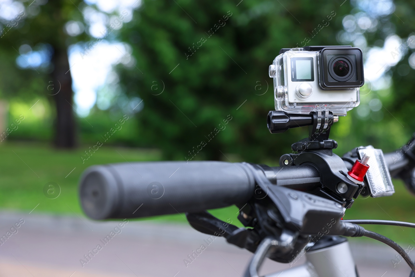 Photo of Modern action camera with mount on bicycle outdoors, closeup