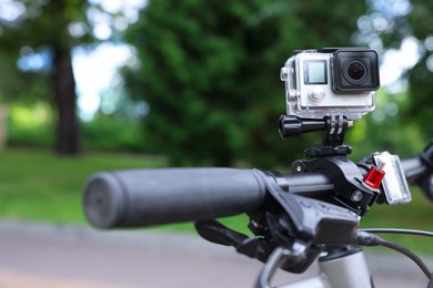 Photo of Modern action camera with mount on bicycle outdoors, closeup