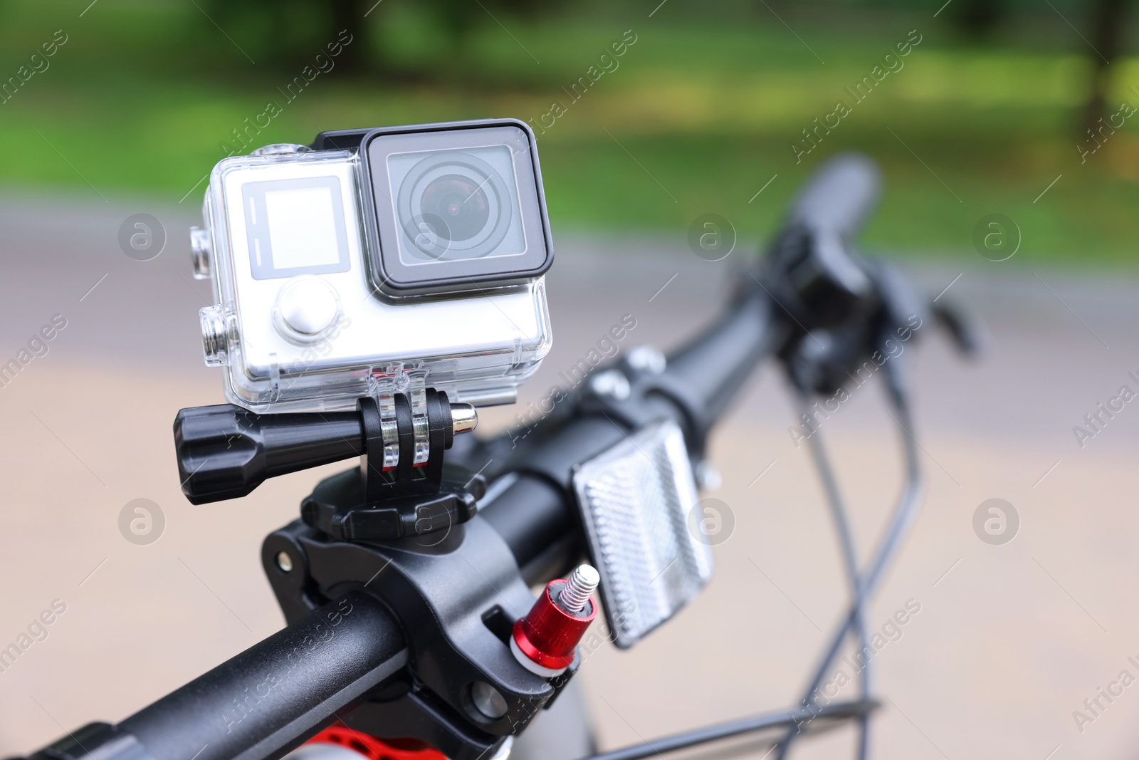 Photo of Modern action camera with mount on bicycle outdoors, closeup