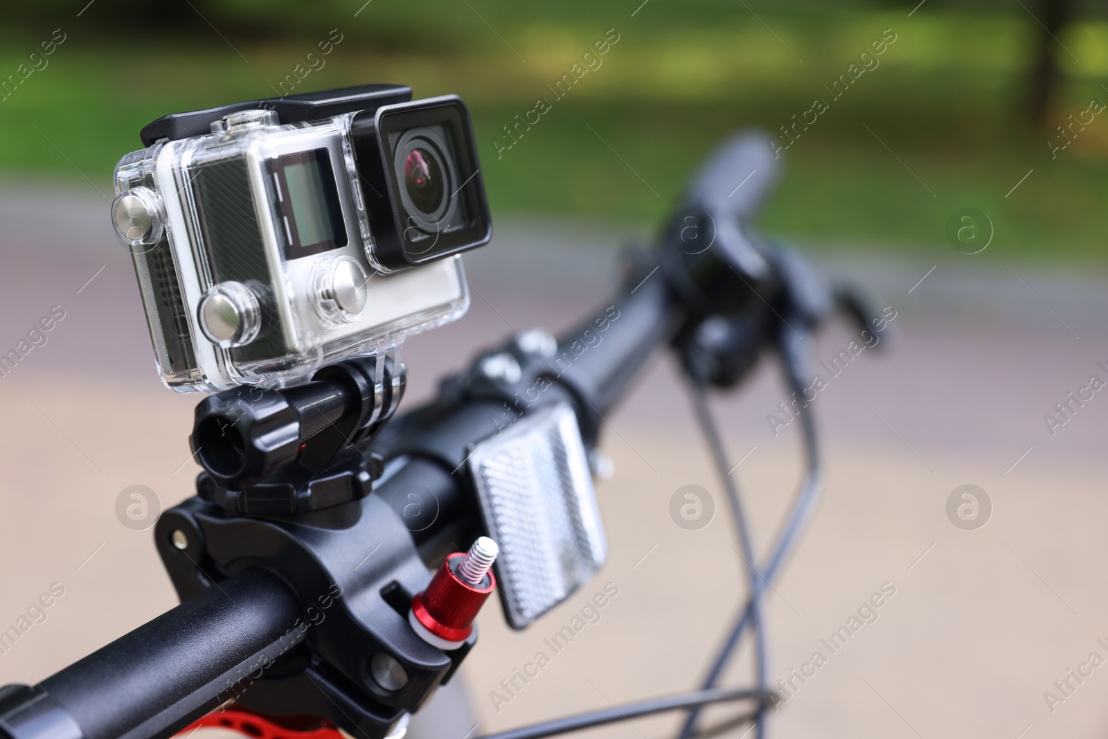 Photo of Modern action camera with mount on bicycle outdoors, closeup. Space for text