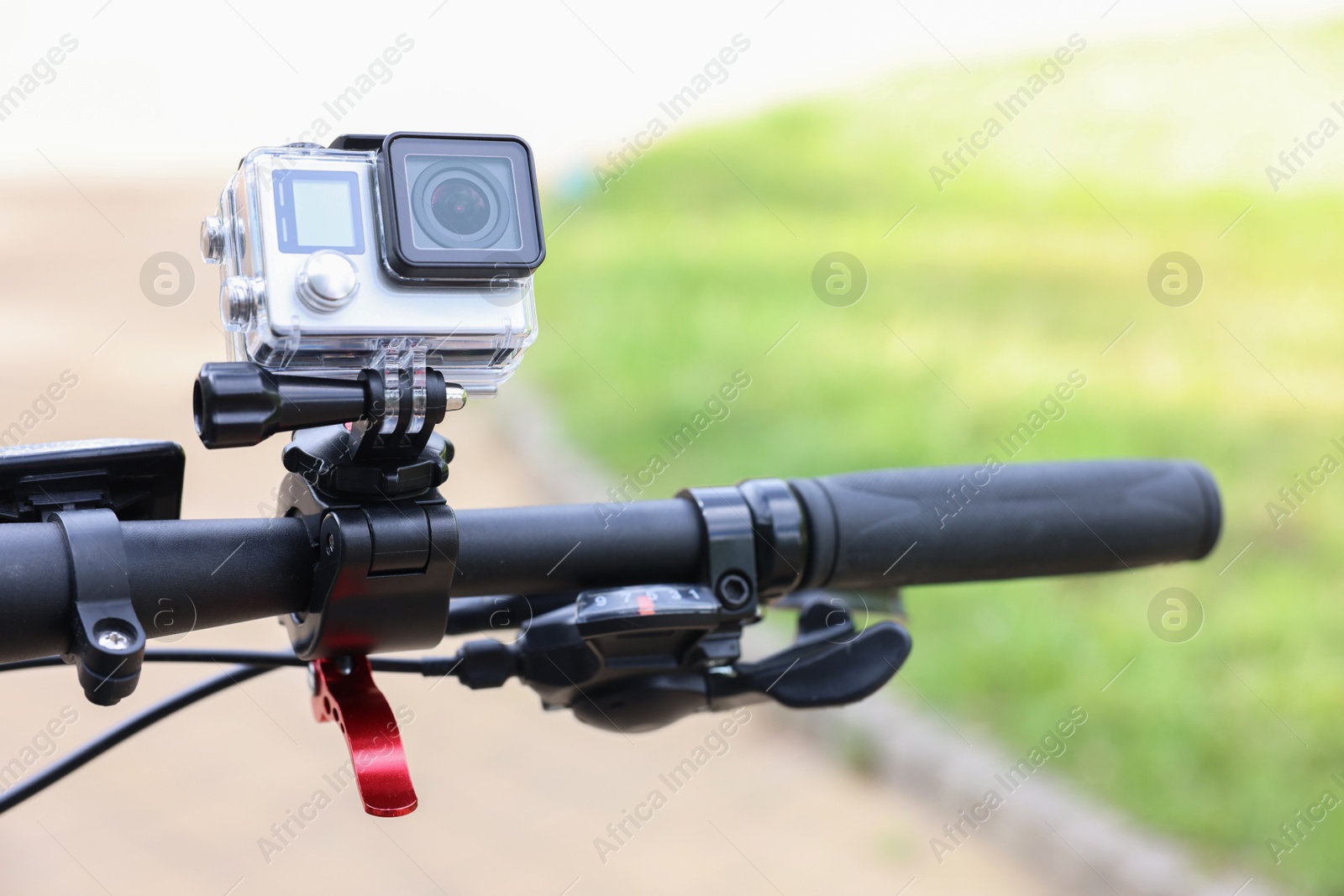 Photo of Modern action camera with mount on bicycle outdoors, closeup