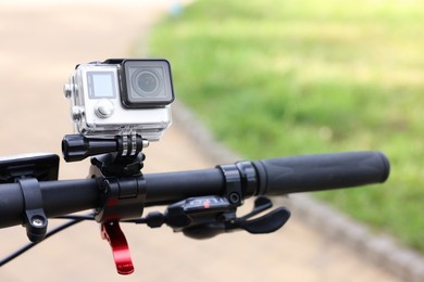 Photo of Modern action camera with mount on bicycle outdoors, closeup