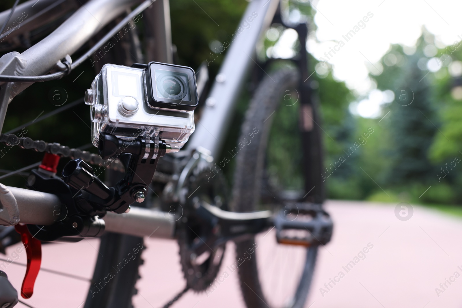 Photo of Modern action camera with mount on bicycle outdoors, closeup. Space for text