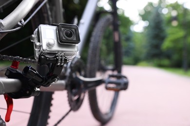 Photo of Modern action camera with mount on bicycle outdoors, closeup. Space for text