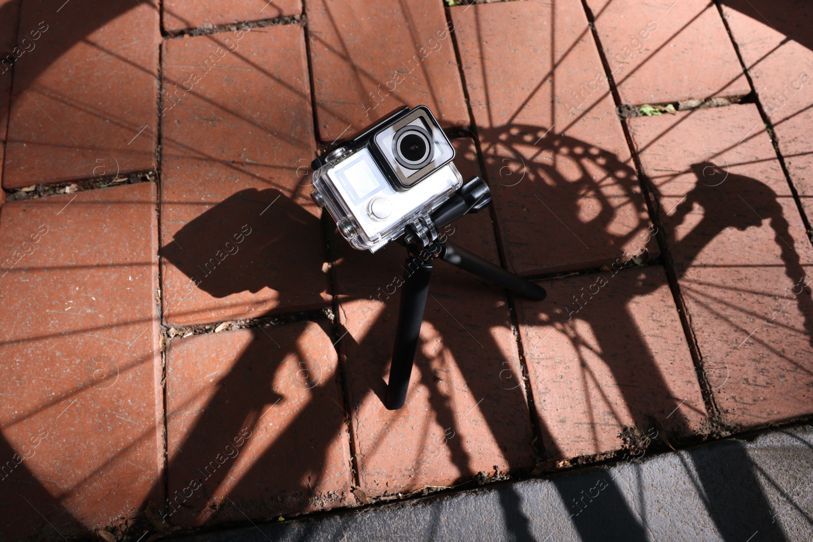 Photo of Modern action camera with tripod on pavement outdoors, above view