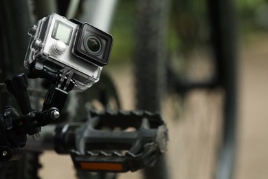 Photo of Modern action camera with mount on bicycle outdoors, closeup. Space for text