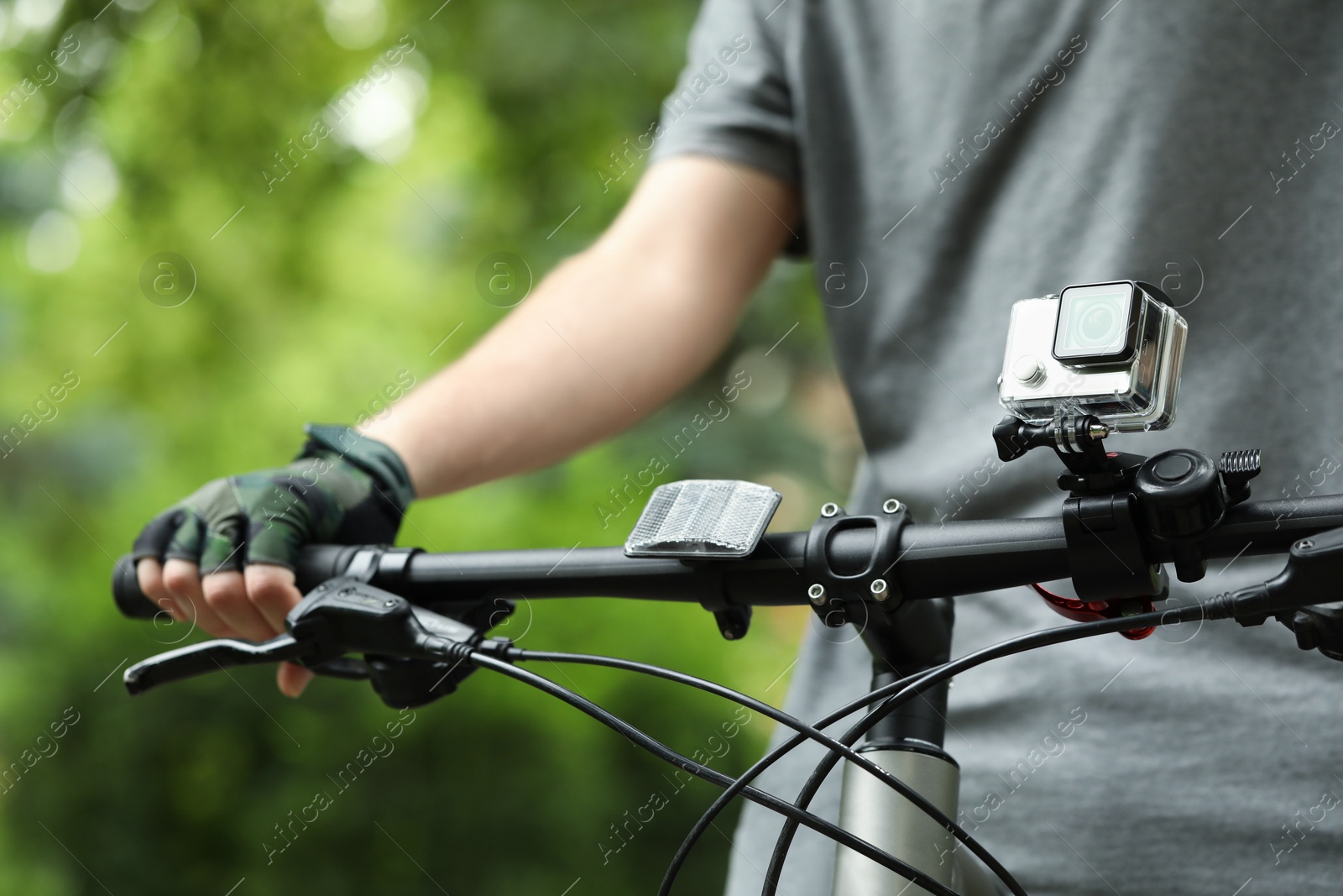 Photo of Man riding bicycle with modern action camera outdoors, closeup