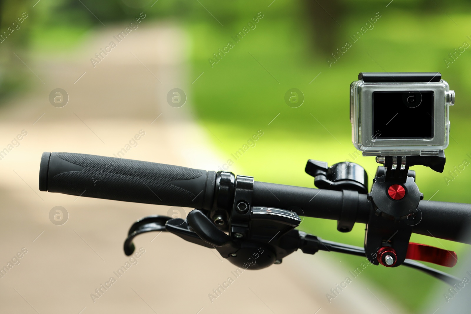 Photo of Modern action camera with mount on bicycle outdoors, closeup