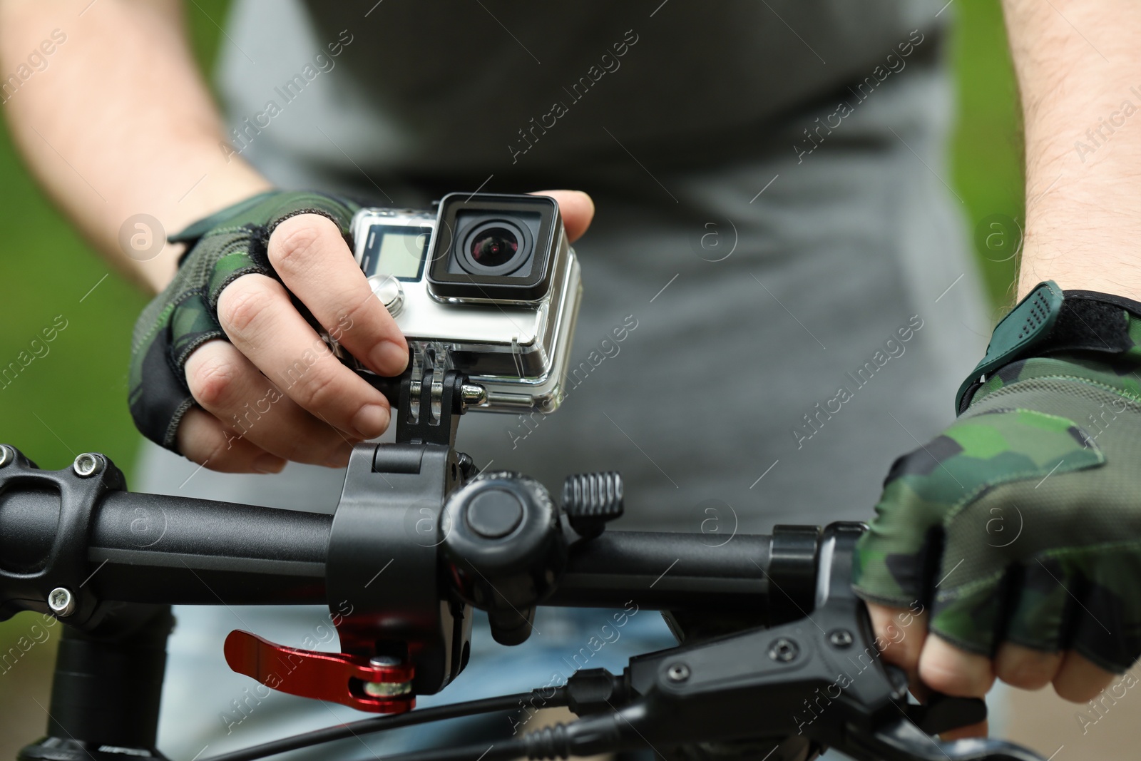 Photo of Man riding bicycle with modern action camera outdoors, closeup