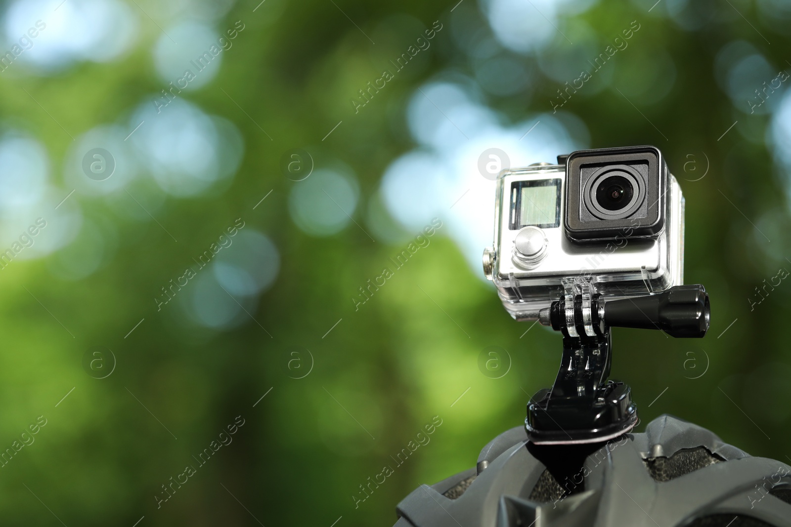 Photo of Modern action camera with mount on helmet outdoors, closeup. Space for text