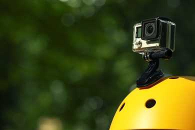 Modern action camera with mount on helmet outdoors, closeup. Space for text