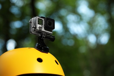 Photo of Modern action camera with mount on helmet outdoors, closeup. Space for text