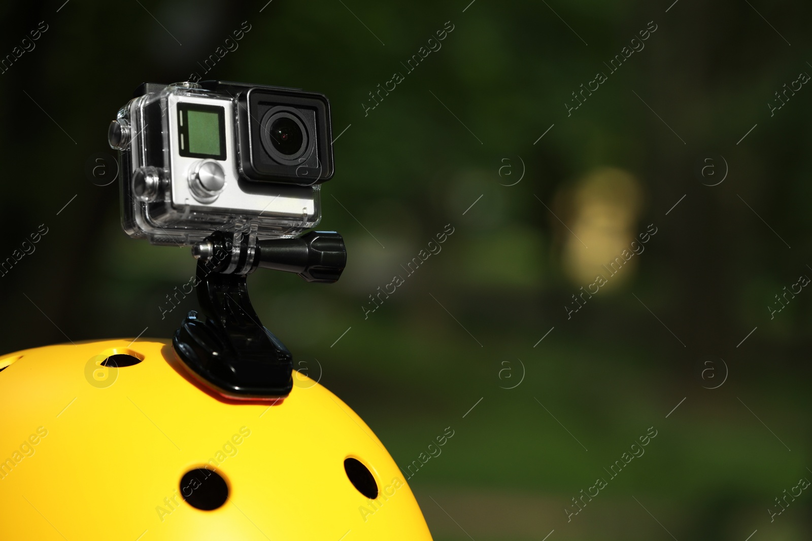 Photo of Modern action camera with mount on helmet outdoors, closeup. Space for text