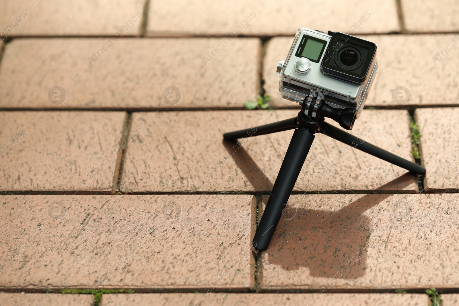 Photo of Modern action camera with tripod on pavement outdoors, space for text