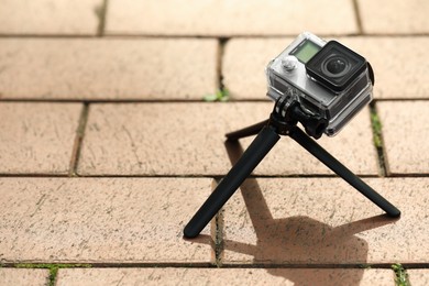 Photo of Modern action camera with tripod on pavement outdoors, space for text