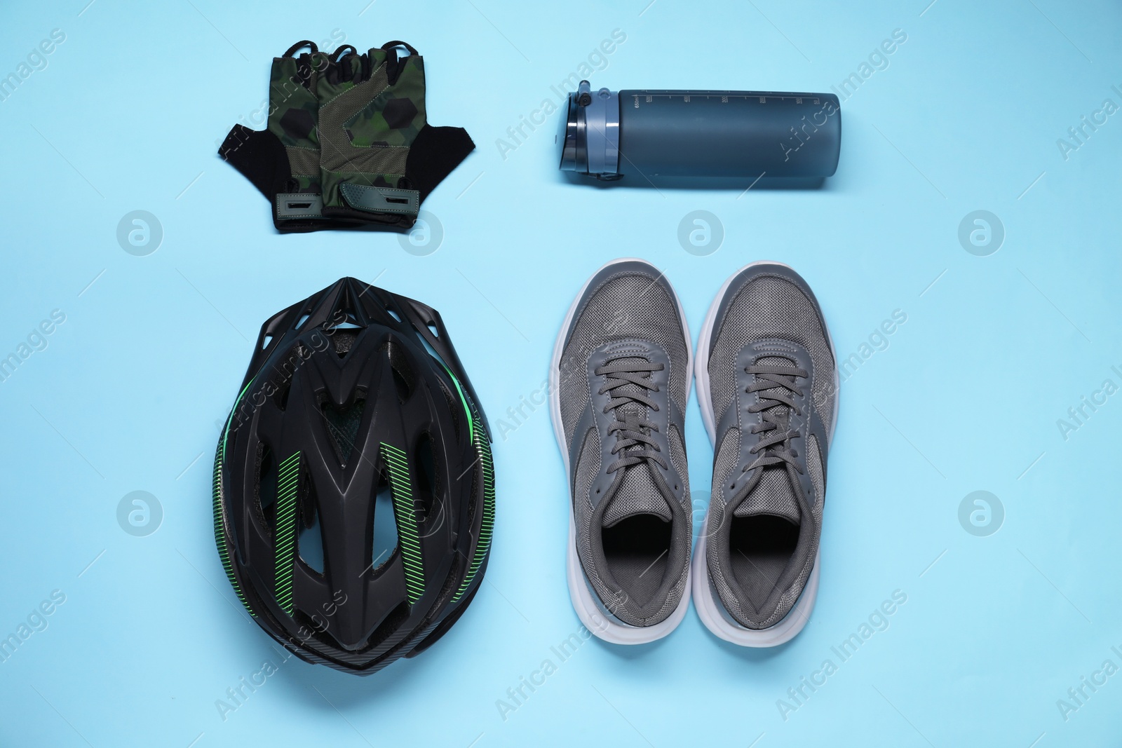 Photo of Bicycle helmet, sneakers, thermo bottle and fingerless gloves on light blue background, flat lay