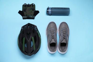 Bicycle helmet, sneakers, thermo bottle and fingerless gloves on light blue background, flat lay