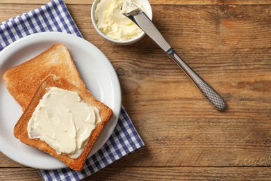 Photo of Delicious toasted bread slices with butter and knife on wooden table, flat lay