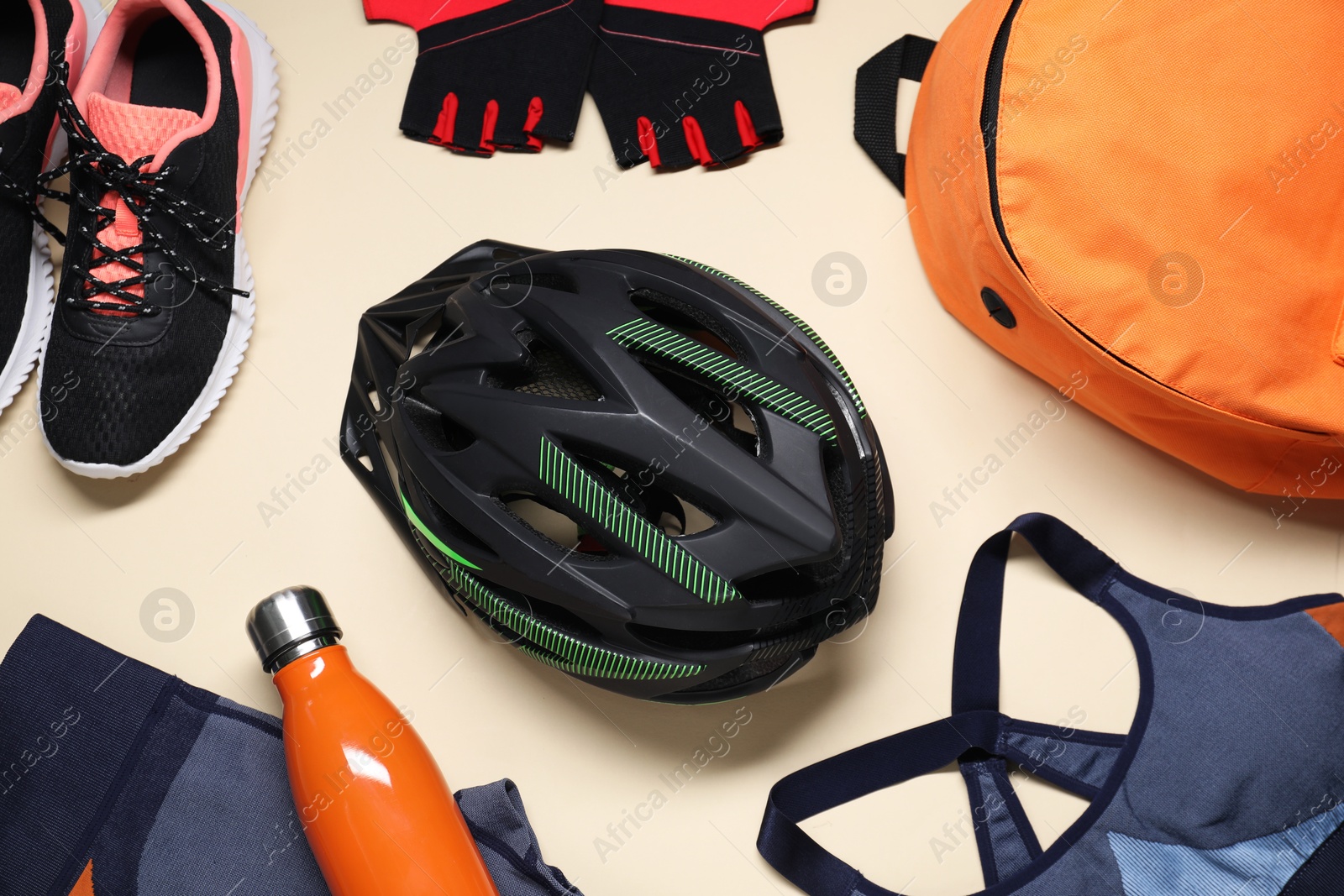 Photo of Bicycle helmet, sportswear, sneakers and bottle on beige background, flat lay