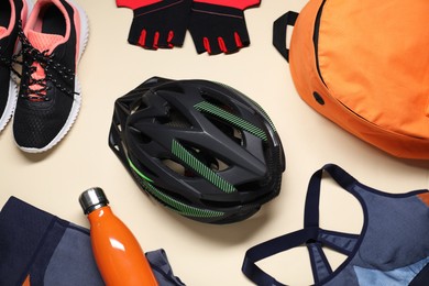 Photo of Bicycle helmet, sportswear, sneakers and bottle on beige background, flat lay