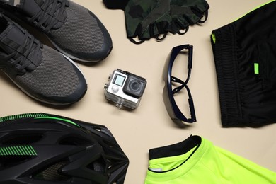 Photo of Bicycle helmet, fingerless cycling gloves, goggles, sportswear and action camera on beige background, flat lay