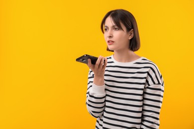 Beautiful woman recording voice message via smartphone on yellow background, space for text