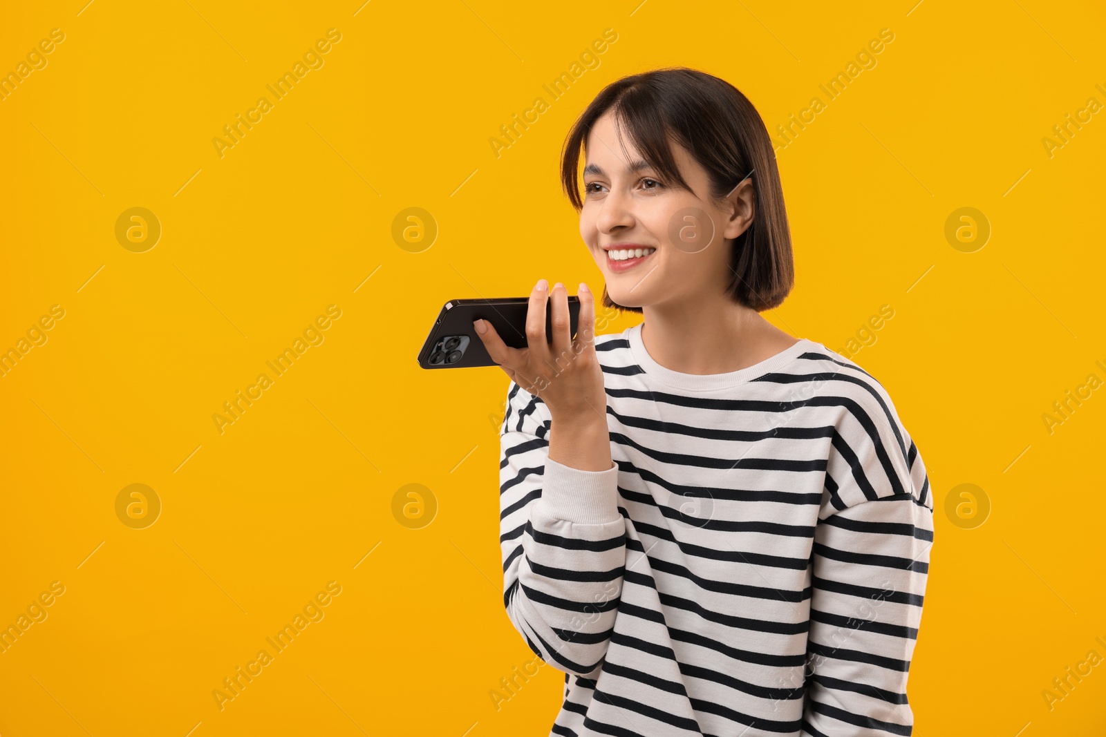 Photo of Beautiful woman recording voice message via smartphone on yellow background, space for text