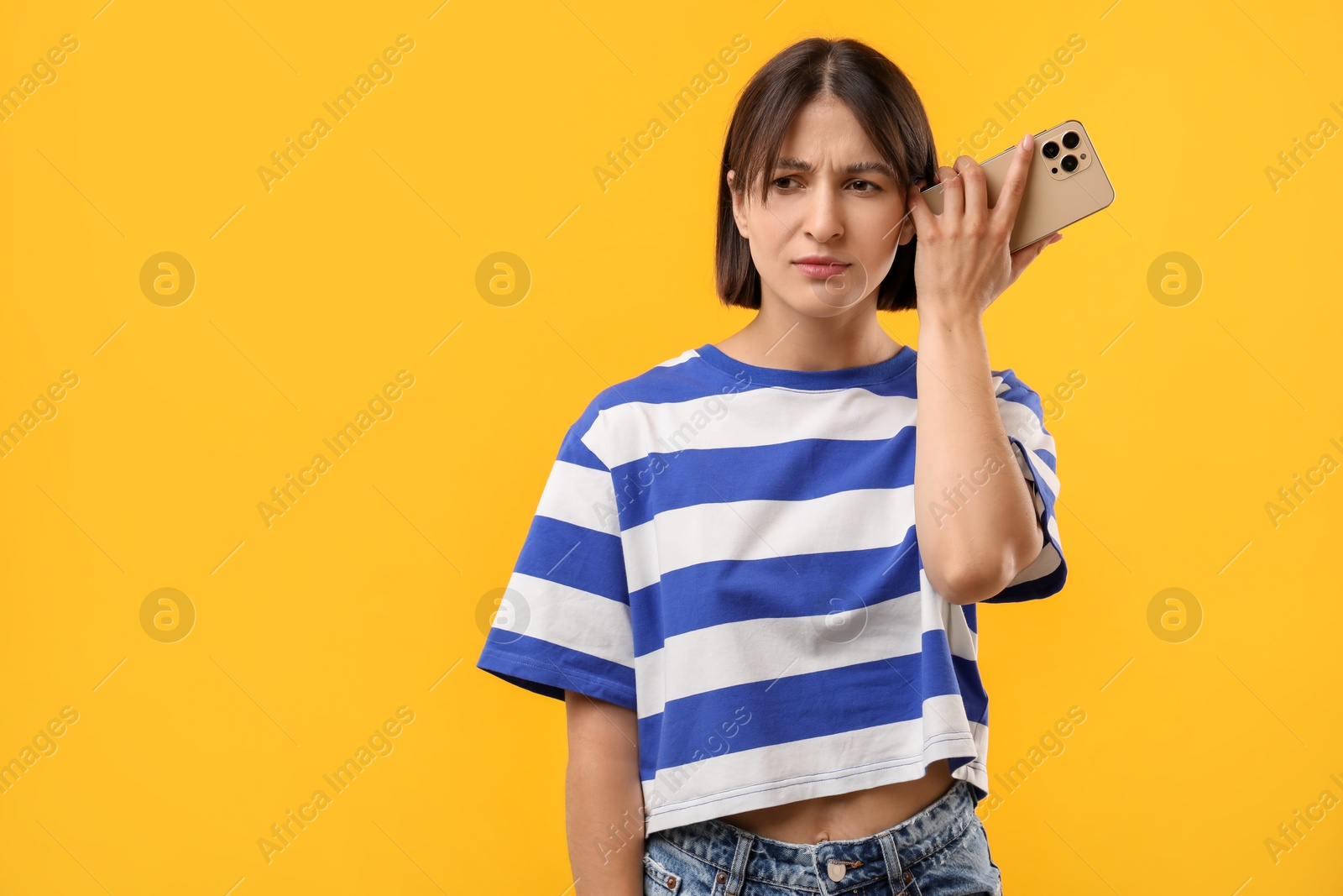 Photo of Beautiful woman with smartphone listening to voice message on yellow background, space for text