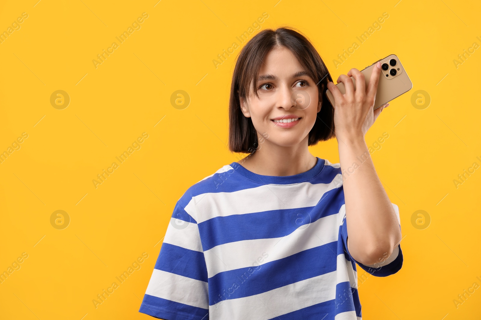 Photo of Beautiful woman with smartphone listening to voice message on yellow background, space for text