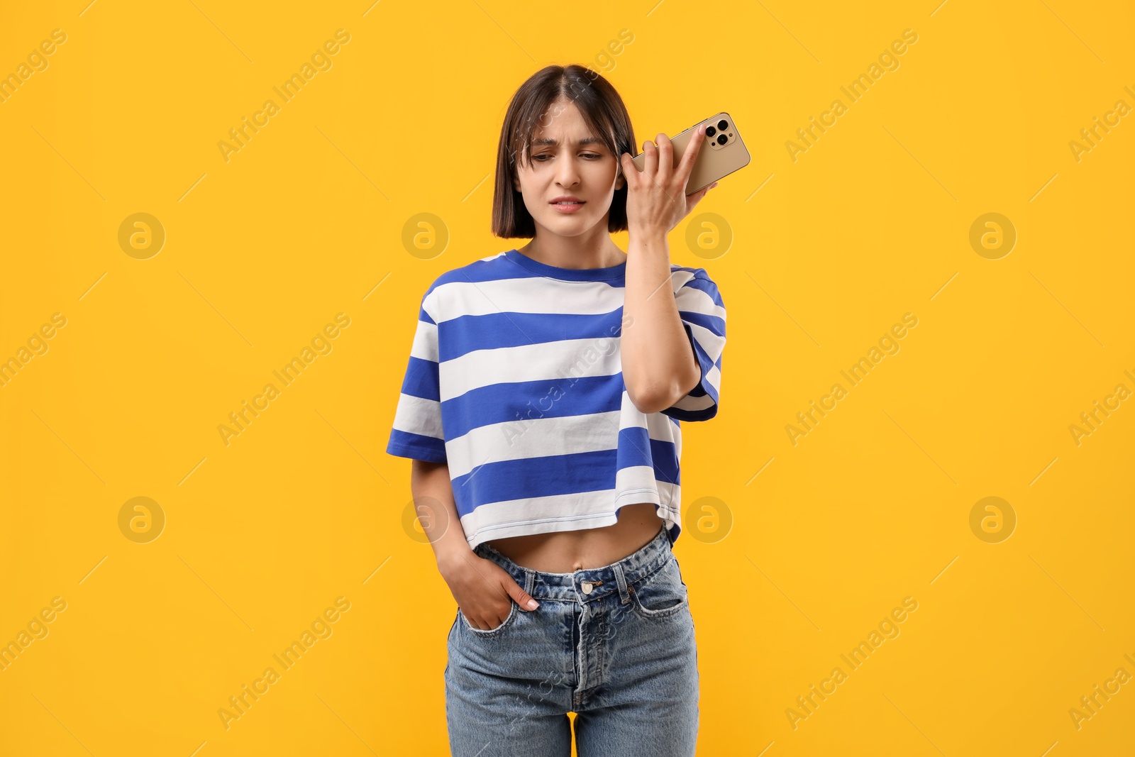 Photo of Beautiful woman with smartphone listening to voice message on yellow background