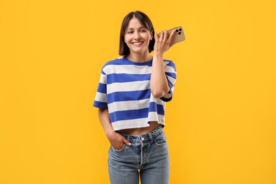 Beautiful woman with smartphone listening to voice message on yellow background