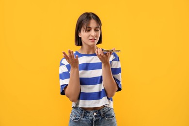 Photo of Beautiful woman recording voice message via smartphone on yellow background