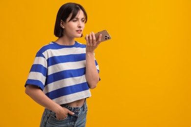 Photo of Beautiful woman recording voice message via smartphone on orange background, space for text