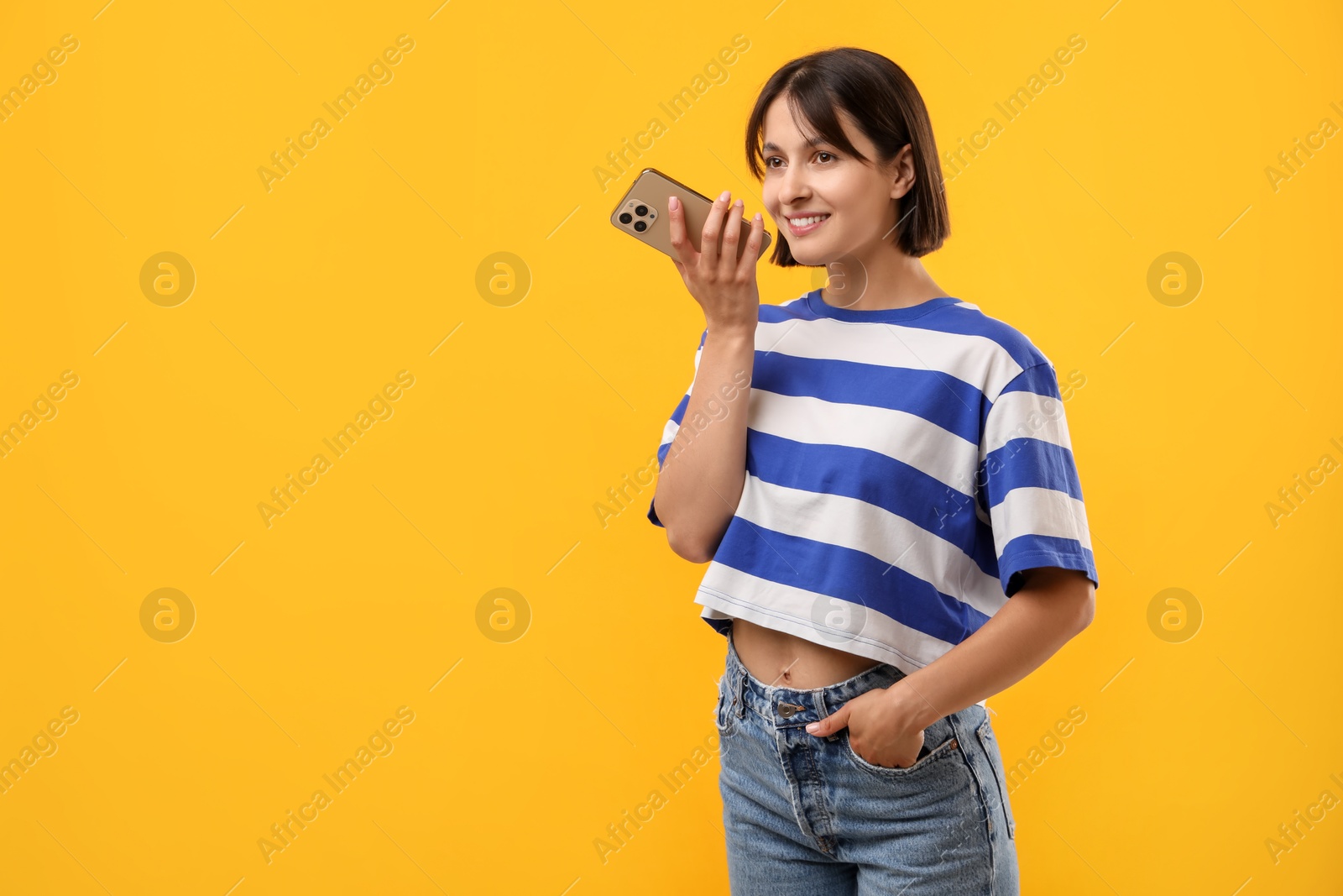 Photo of Beautiful woman recording voice message via smartphone on yellow background, space for text