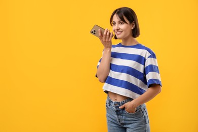 Photo of Beautiful woman recording voice message via smartphone on yellow background, space for text