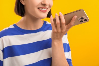 Woman recording voice message via smartphone on yellow background, closeup