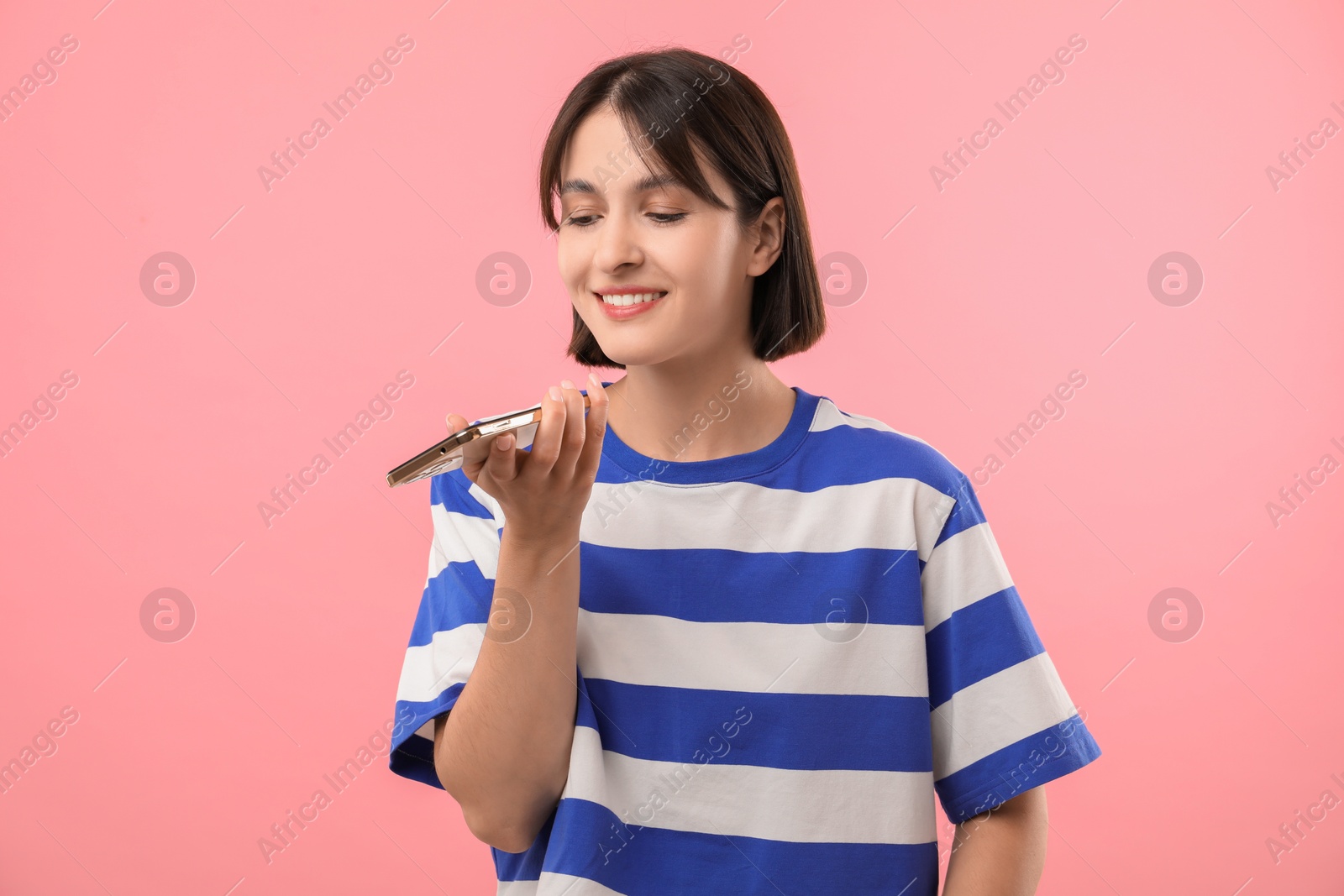 Photo of Beautiful woman recording voice message via smartphone on pink background