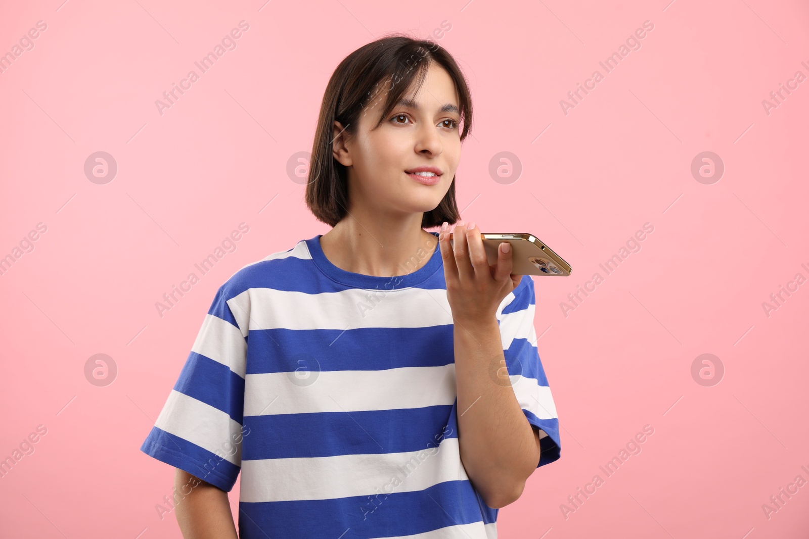 Photo of Beautiful woman recording voice message via smartphone on pink background