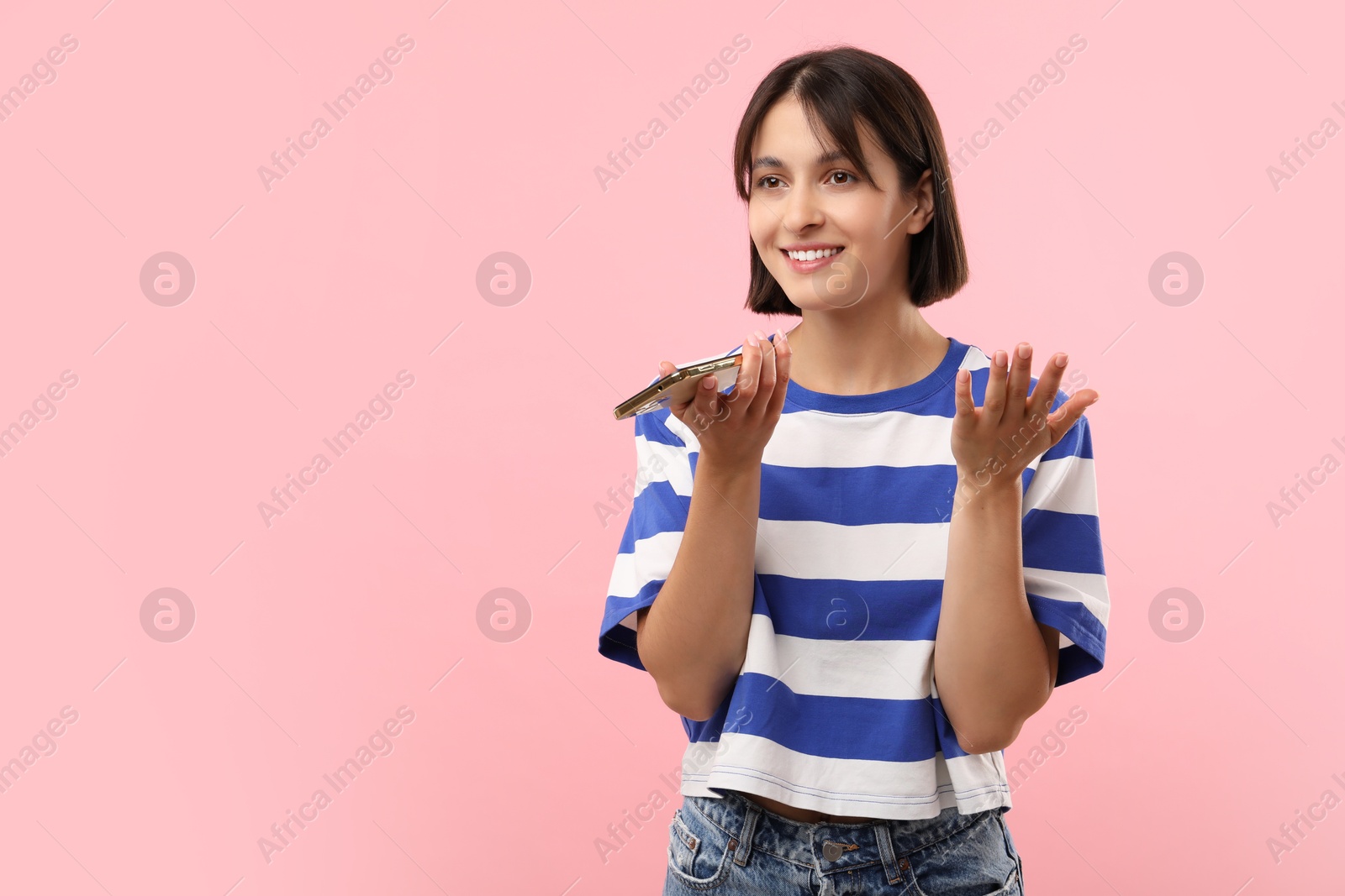 Photo of Beautiful woman recording voice message via smartphone on pink background, space for text