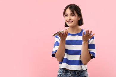 Beautiful woman recording voice message via smartphone on pink background, space for text