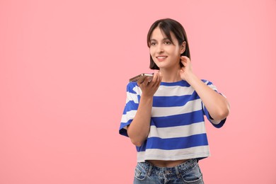 Photo of Beautiful woman recording voice message via smartphone on pink background, space for text