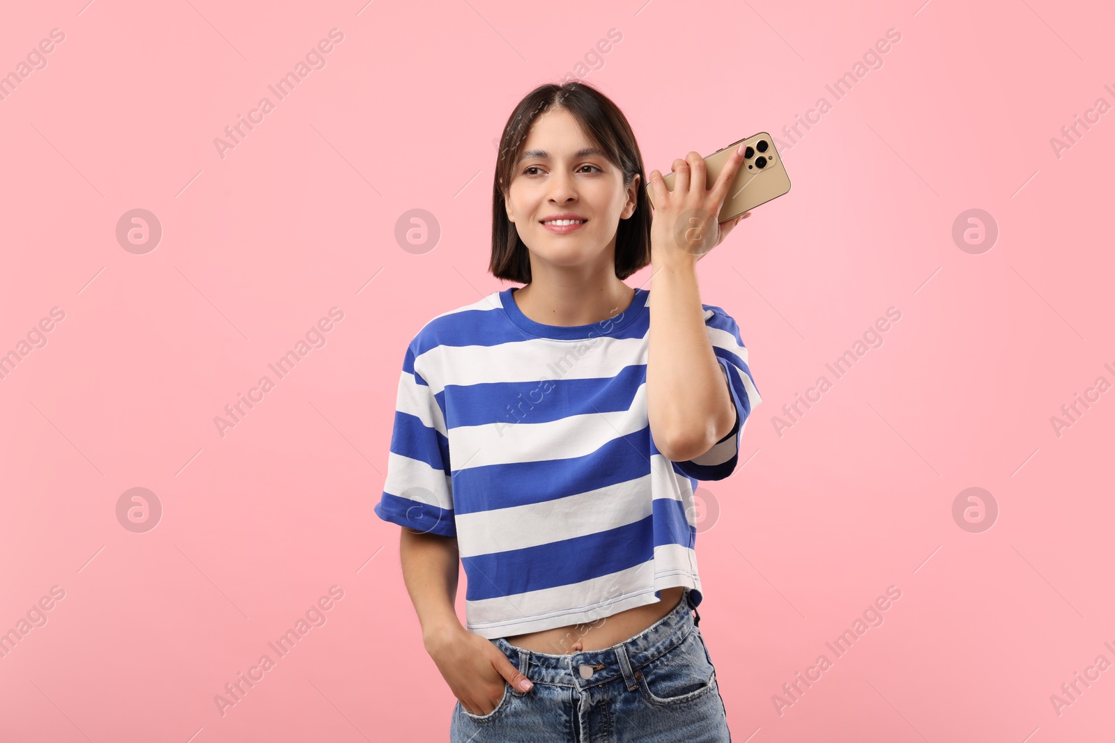 Photo of Beautiful woman with smartphone listening to voice message on pink background