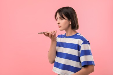 Photo of Beautiful woman recording voice message via smartphone on pink background, space for text