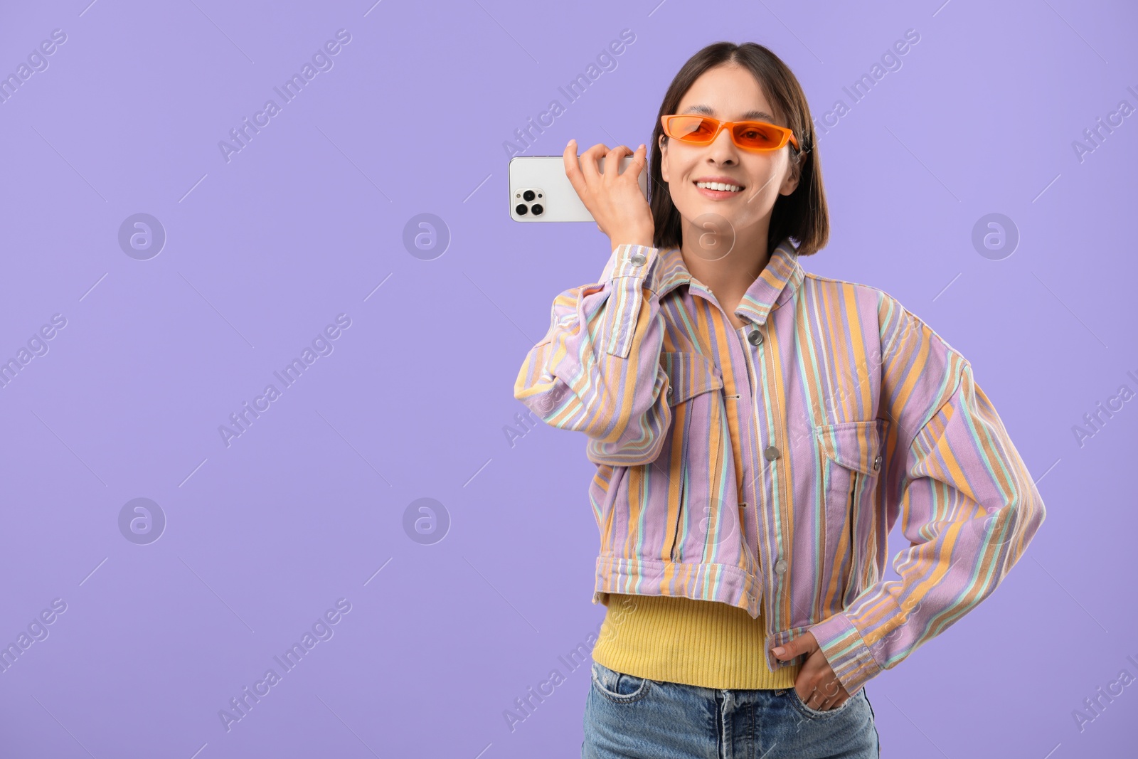 Photo of Beautiful woman in sunglasses with smartphone listening to voice message on violet background, space for text