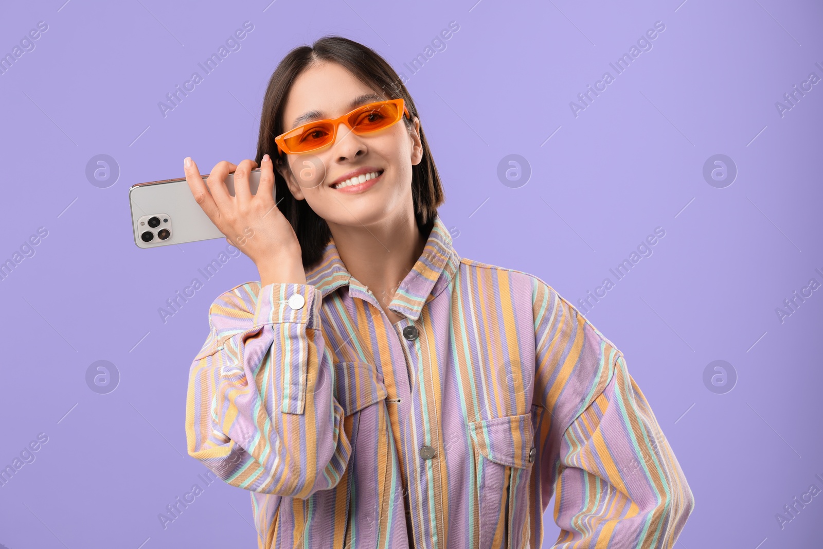 Photo of Beautiful woman in sunglasses with smartphone listening to voice message on violet background