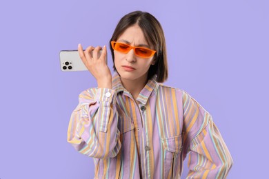 Photo of Beautiful woman in sunglasses with smartphone listening to voice message on violet background