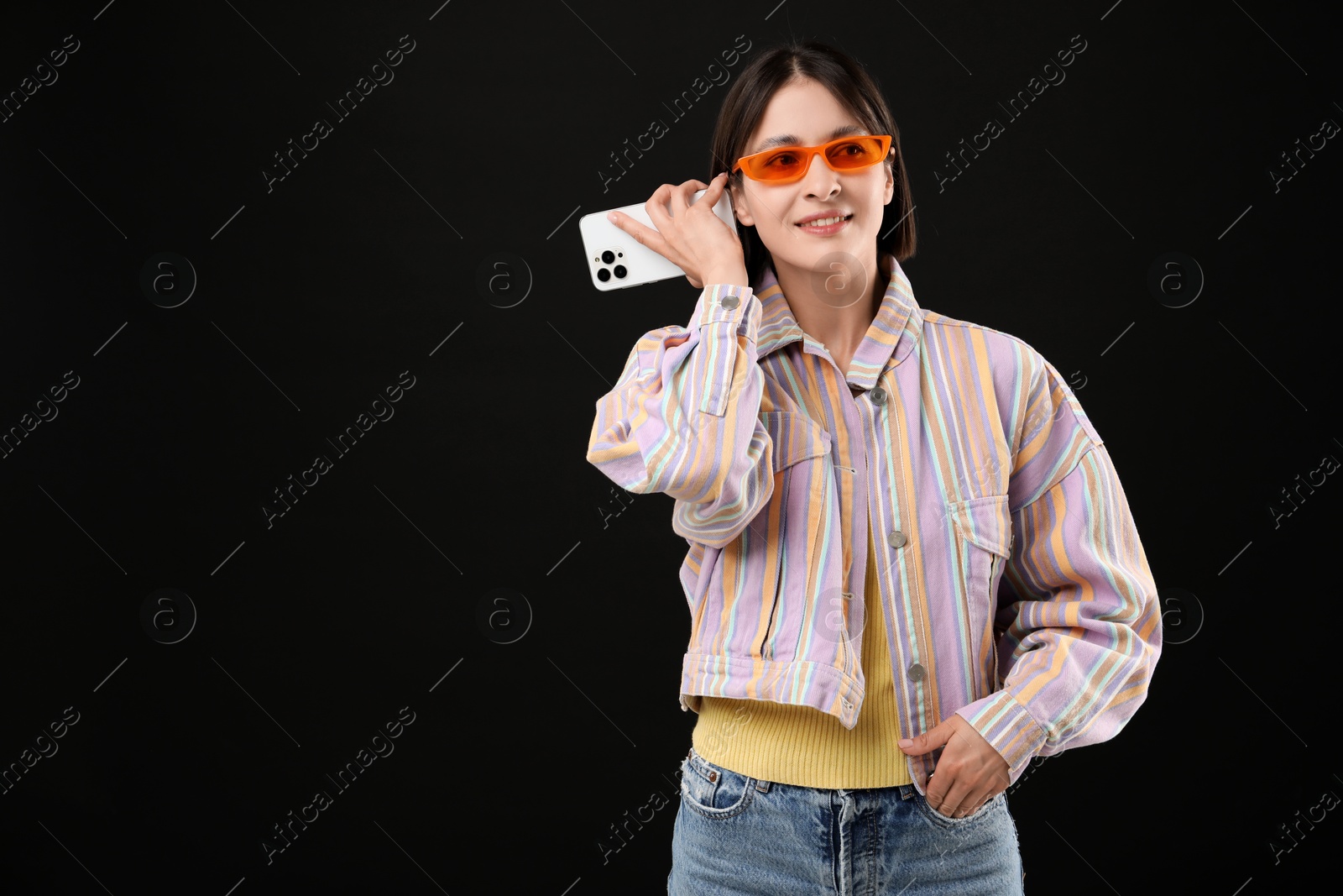 Photo of Beautiful woman in sunglasses with smartphone listening to voice message on black background, space for text